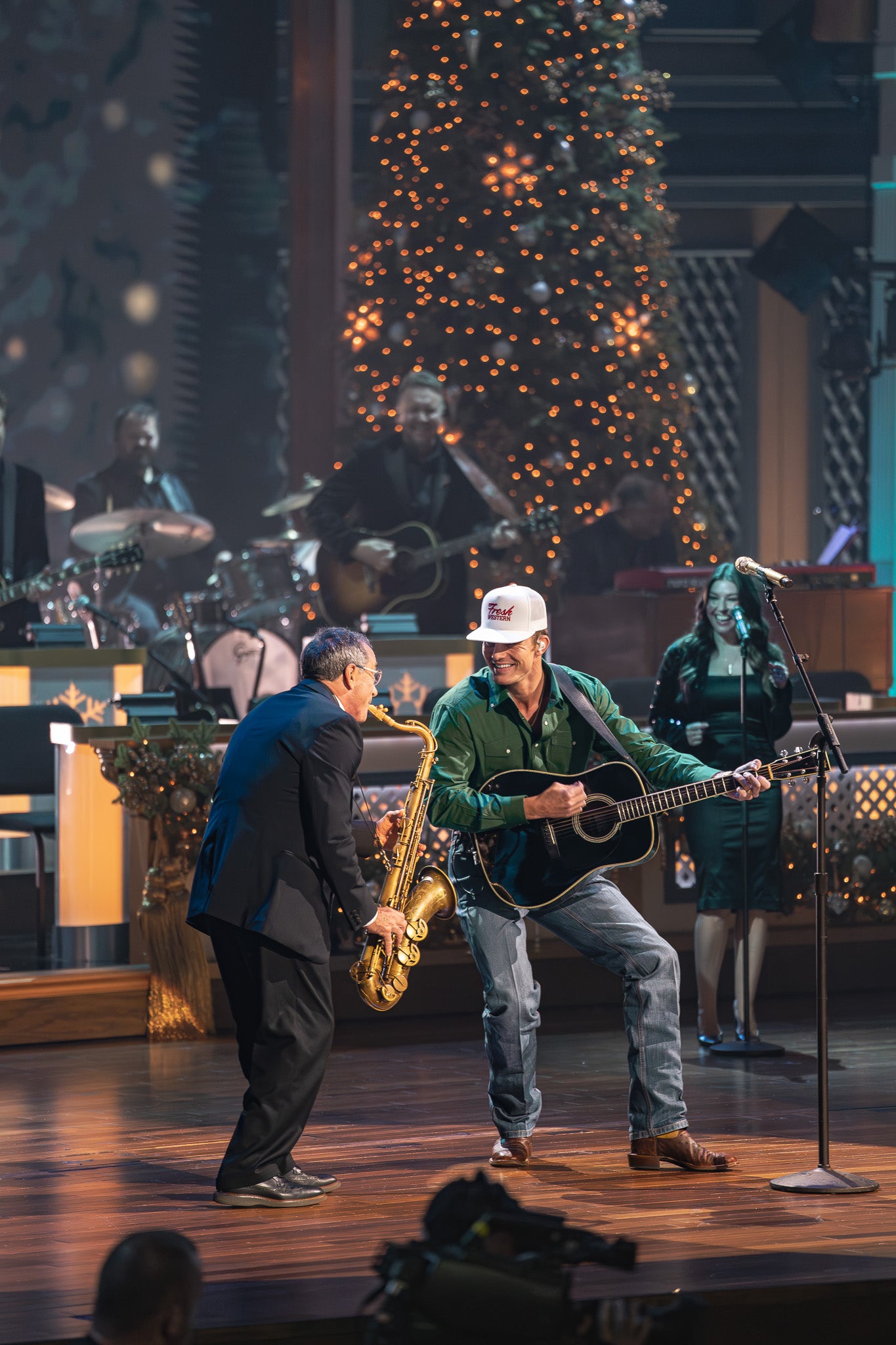 Two musicians performing on stage with a Christmas tree in the background